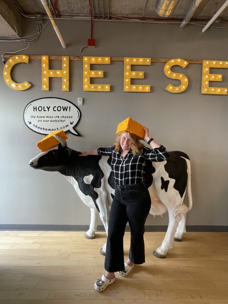 Morgen posing in front of a cow statue, wearing a "cheesehead" hat at the Wisconsin Cheese Mart