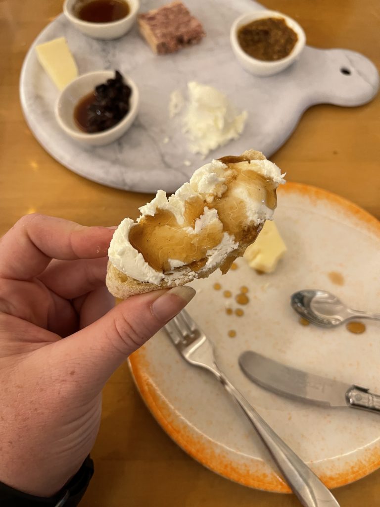 A close-up shot of a cheeseboard bite - fresh chevre on a crostini with some house-made spiced honey - from Beautiful Rind in Chicago!