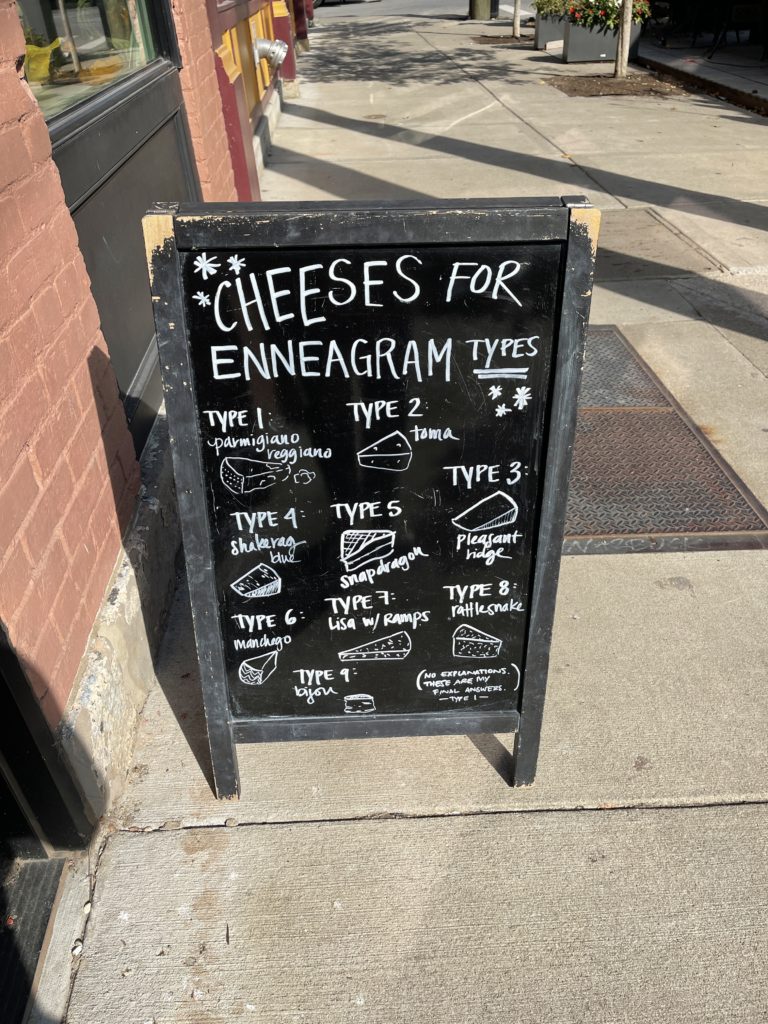 A sandwich board sign outside of The Rhined showing "cheeses for enneagram type"