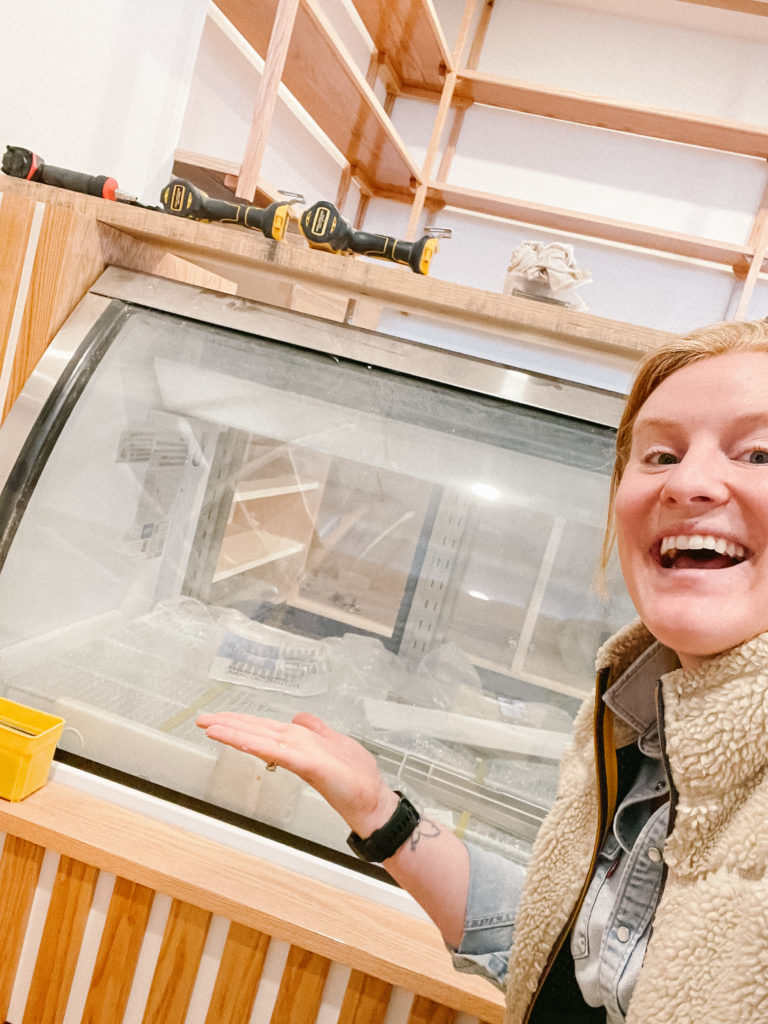 Morgen smiling in front of an empty cheese case, brimming with possibilities