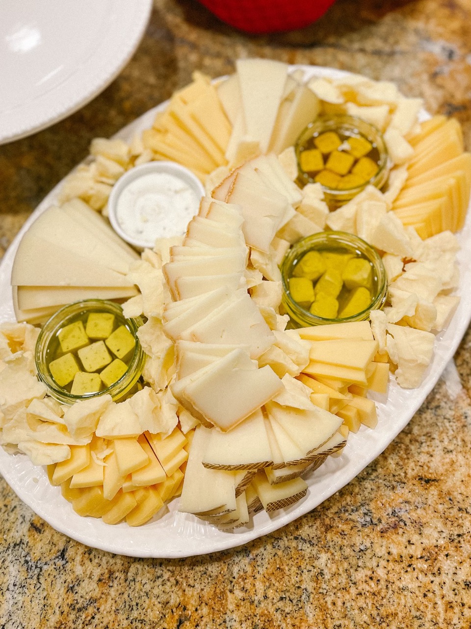 A large oval plate of cheese, featuring slices of gouda, manchego, cheddar and marinated feta in olive oil and herbed goat cheese.