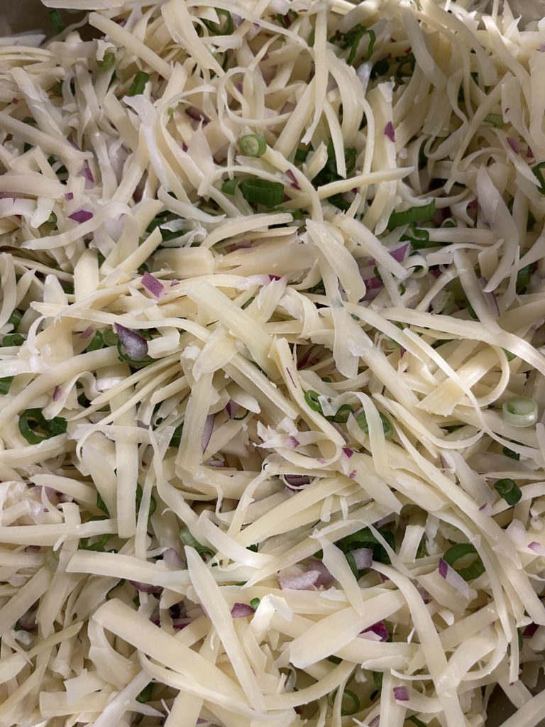Up close and personal with Jarlsberg cheese dip in progress. A close-up photo of shredded Jarlsberg cheese, red onion, and green onion mix.