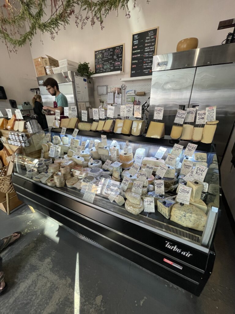 A photo of the cheese case at the Cheese Shop of Portland, showing a wide variety of cheeses.